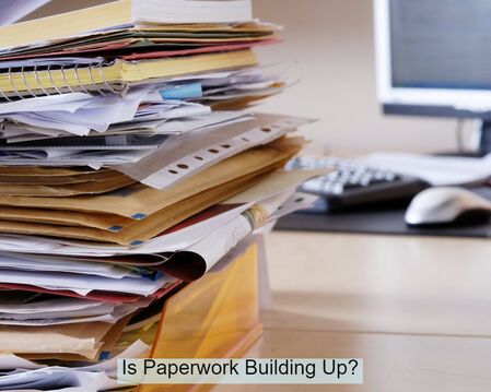 Picture of stacked, unsorted paperwork within an office.